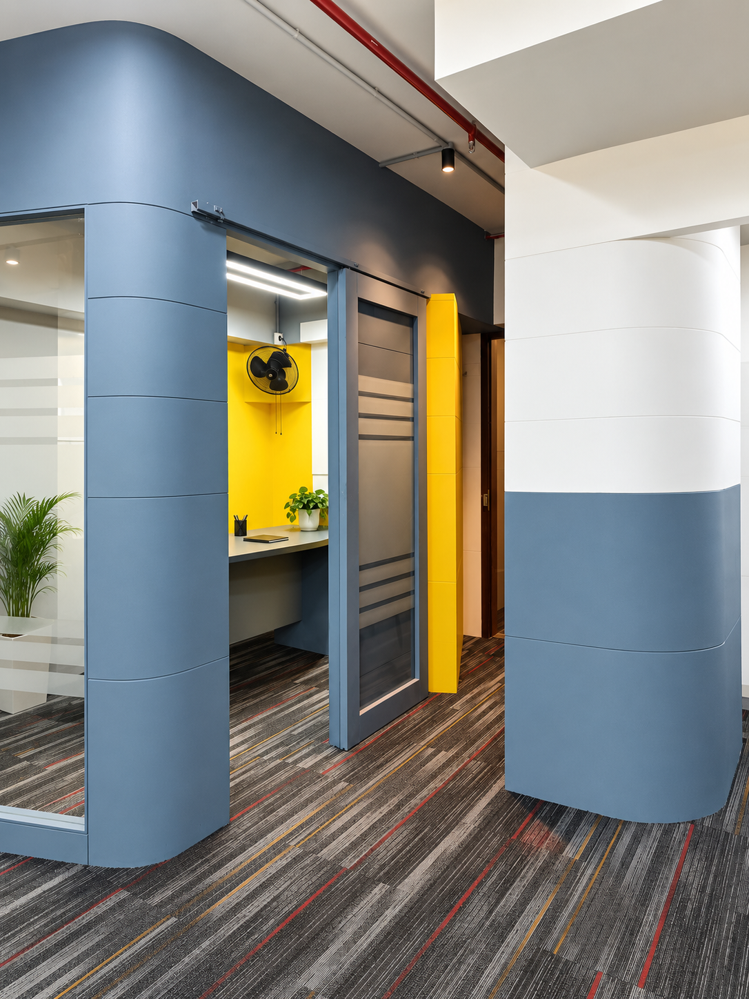Office corridor with a blue-grey curved wall opening into a compact startup workspace