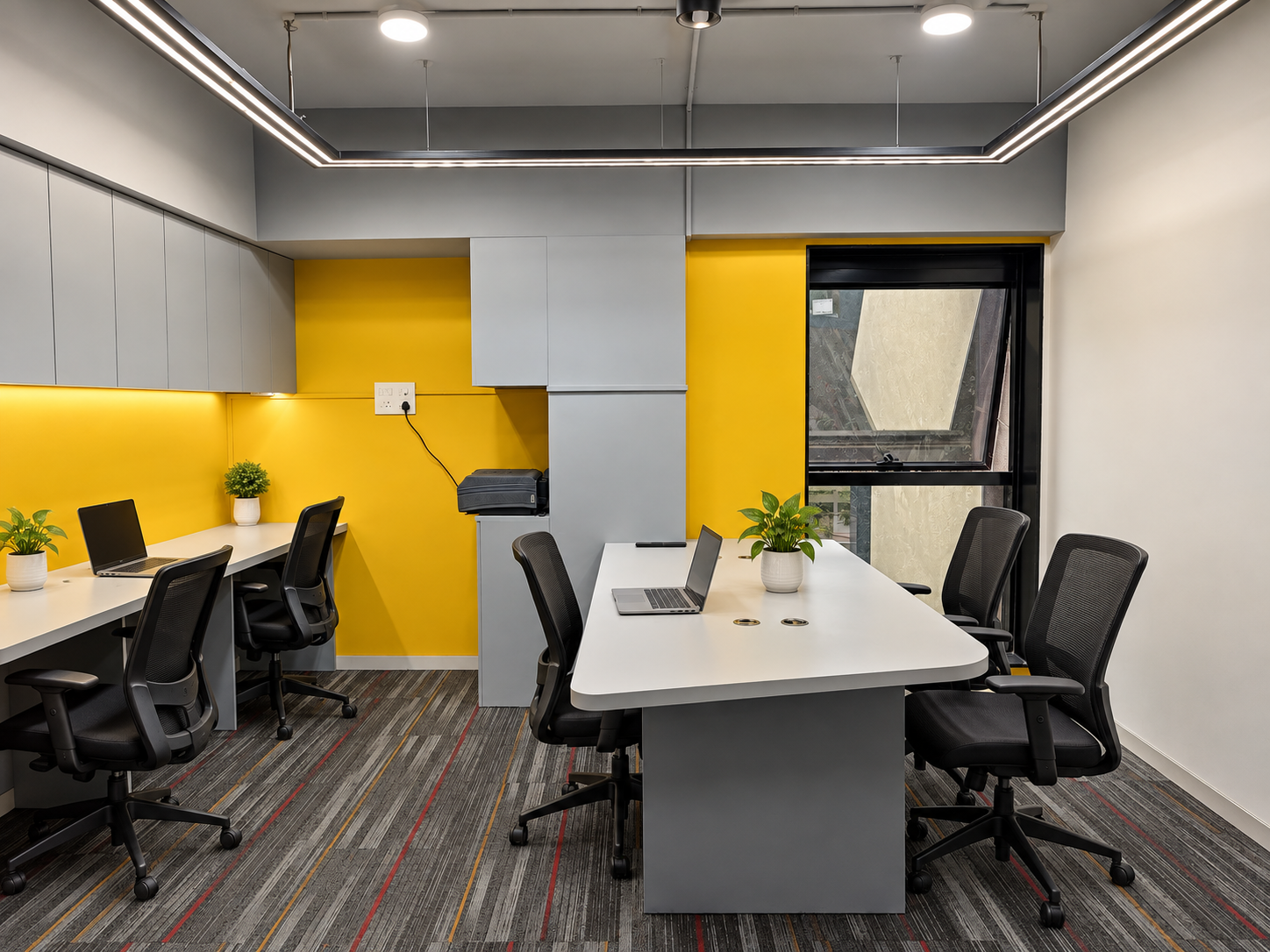 Main workspace with a perimeter desk, central table, yellow accent wall and dark commercial carpet