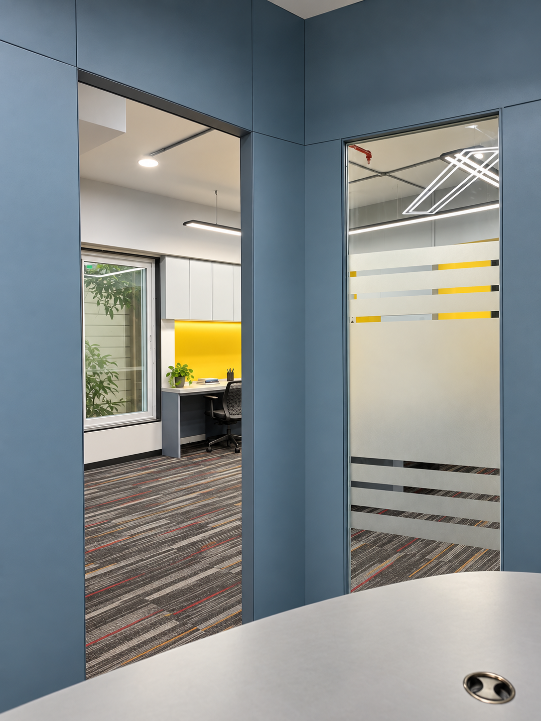 Layered view through a blue-grey doorway into a bright office with desk, window and greenery
